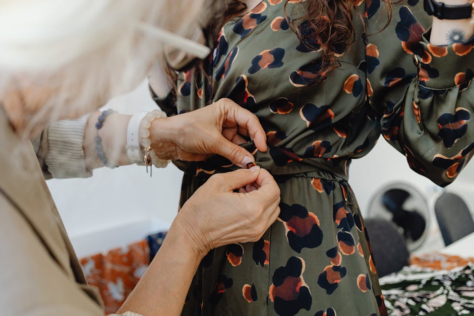 A seamstress closely adjusts a stylish patterned dress at waist level indoors.